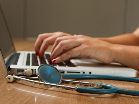 person sitting while using laptop computer and green stethoscope near